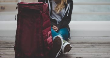 Au pair Rematch Frau sitzt auf dem Boden mit gepacktem Rucksack im Vordergrund