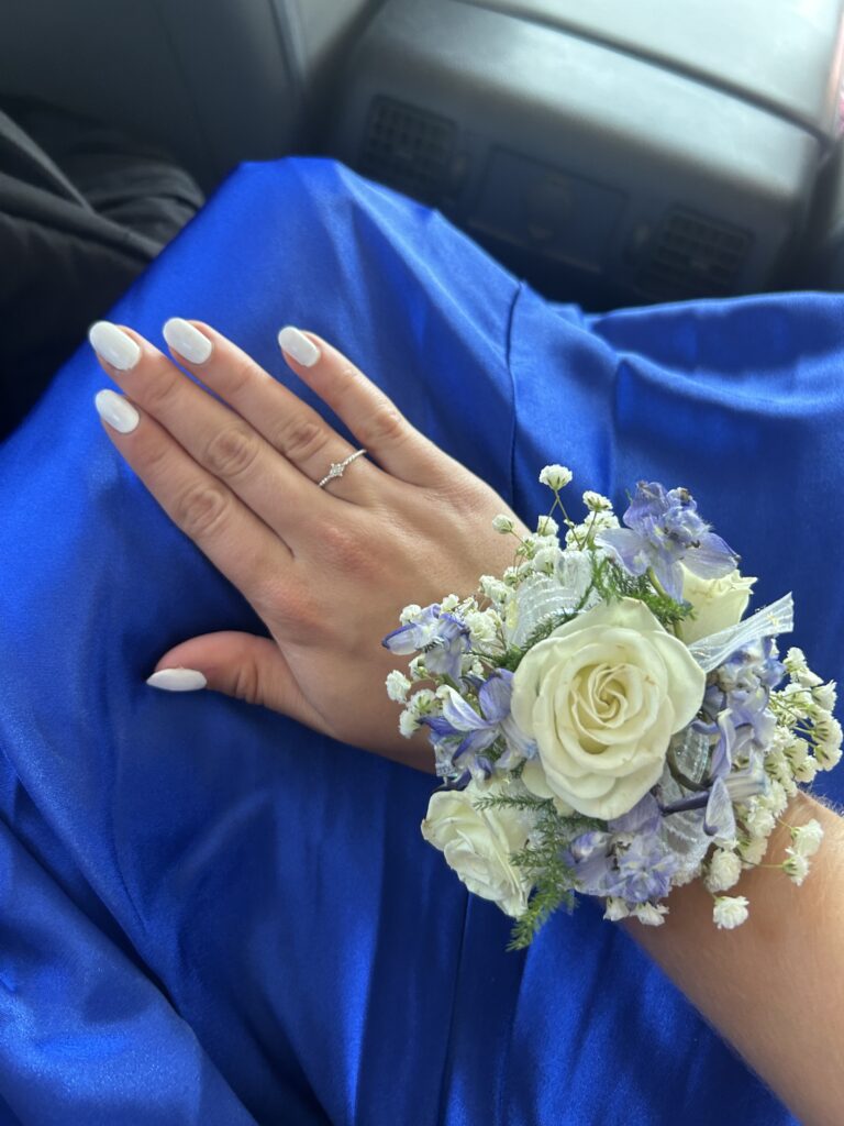 Hand mit Blumenarmband und blauem Kleid