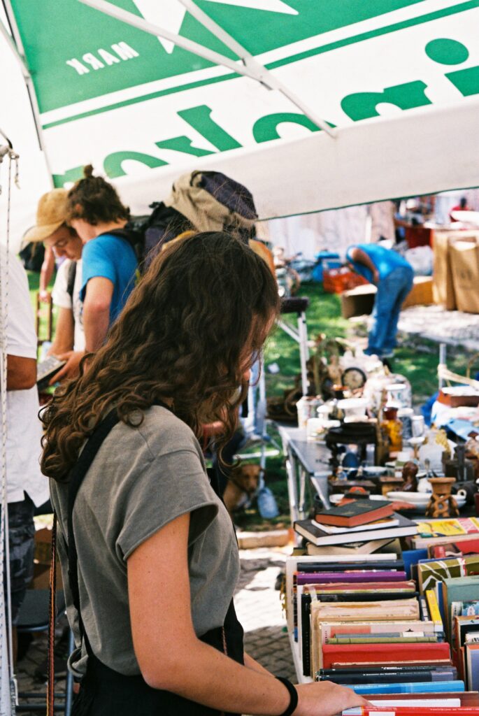 junge frau schaut sich eine kiste mit büchern auf einem flohmarkt an