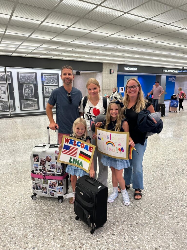 lina mit ihren gasteltern und gastschwestern mit welcome-schildern bei der begrüßung am flughafen