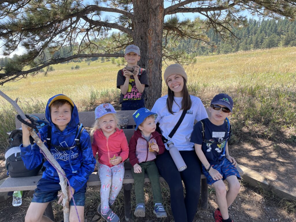 Au pair sitzt draußen bei einer Wanderung mit fünf Kindern auf einer Bank