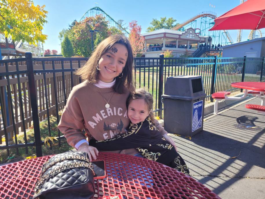 au pair mit ihrem gastkind im freizeitpark mit achterbahnen im hintergrund