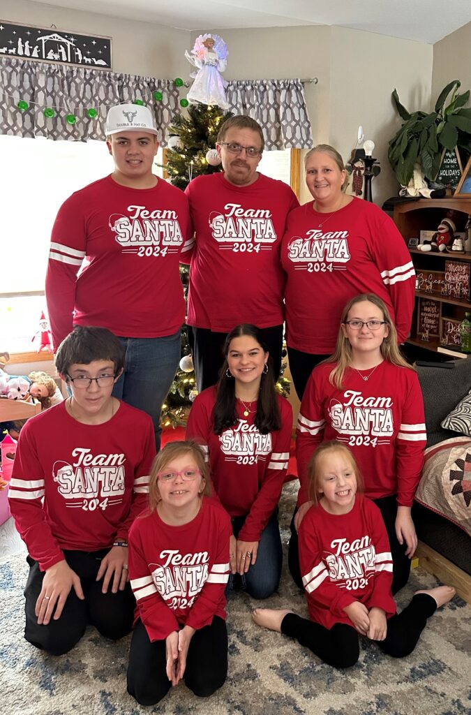 Gruppenfoto von Paulinas Gastfamilie vor dem Weihnachtsbaum, alle tragen identische Weihnachtsschlafanzüge mit "Team Santa" drauf.