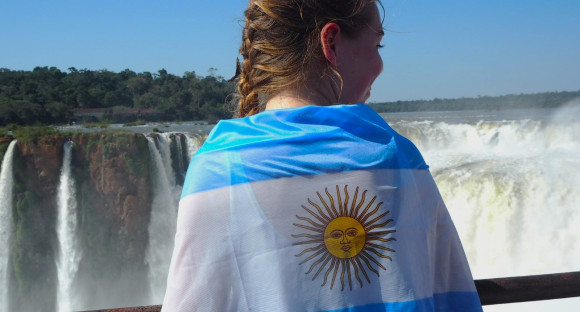 Schülerin von hinten mit Argentinien Flagge über die Schultern vor einem Wasserfall